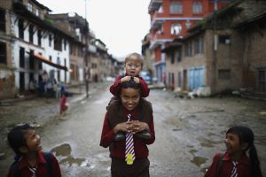 A boy carries a child on his back as they return home from school along the streets of Lalitpur